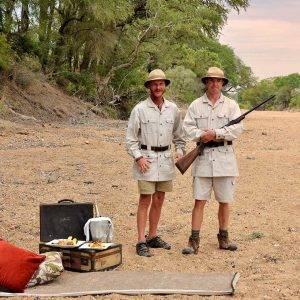 Hamiltons Tented Camp - 2 men dressed in nostalgic pith helmets and dressed in old fashioned safari clothes holding a rifle.