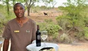 Imbali-Safari-Lodge - Black man welcoming guests with a bottle of wine and glass on a tray